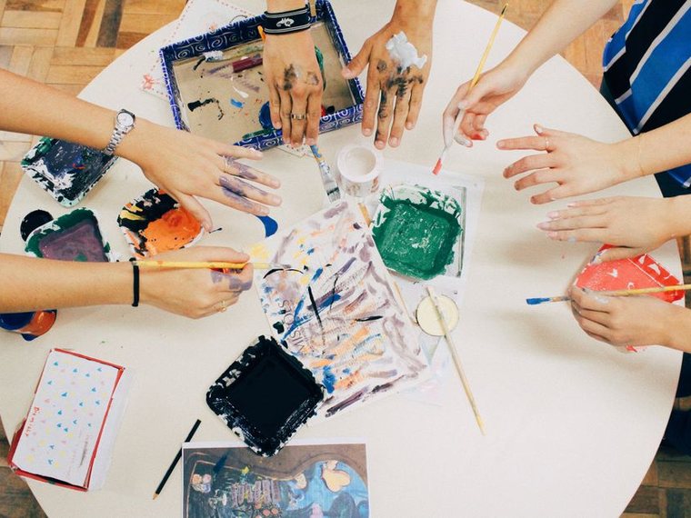 Mains autour d'une table couverte de peintures et d'outils créatifs
